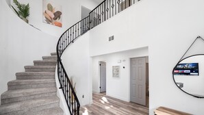 A staircase with a black railing leading to a second floor, a wooden bench, and a wall-mounted TV. - Casa Yucca 1 (Chandler)