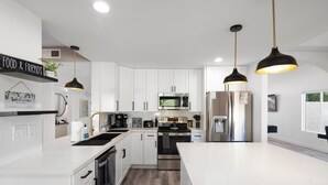 A modern kitchen with white cabinetry, stainless steel appliances, and pendant lighting. - Casa Yucca 1 (Chandler)