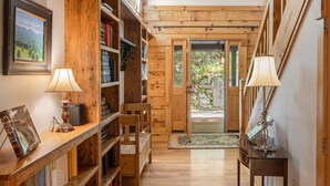Una biblioteca amplia con estanterías de madera, un rincón de lectura con sillas y un gran ventanal con vistas al verdor.