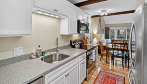 Una cocina moderna con armarios blancos, un refrigerador de acero inoxidable y un comedor con sillas y una mesa de madera.