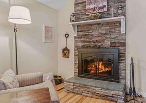 A cozy living room with a stone fireplace, a sofa, a coffee table, and a floor lamp. - New Ski Mtn Condo, Walk to Ski Hill - Kingswood 6C (Quechee)