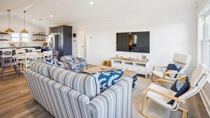 En moderne stue med en stor sofa, et fjernsyn og et spiseområde med et køkken i baggrunden.