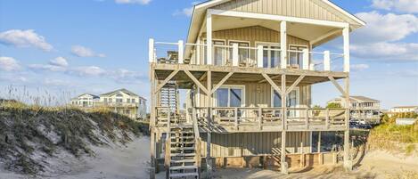 A wooden beach house with a balcony and a staircase leading to the upper level.