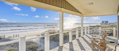 A wooden deck with chairs overlooking a beach.