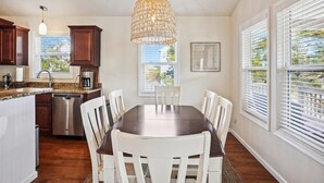 A modern kitchen with dark wood cabinets, stainless steel appliances, and a large dining table with white chairs.