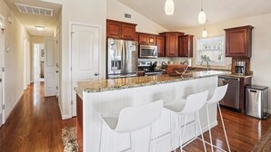 A modern kitchen with granite countertops, stainless steel appliances, wooden cabinets, and pendant lighting.