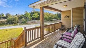 A wooden porch with a bench and a welcome sign, overlooking a road and greenery.