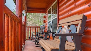 A wooden porch with benches and a railing, overlooking a forested area.
