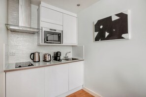 A modern kitchen with white cabinetry, a stainless steel range hood, a microwave, a kettle, a coffee maker, and a sink. - Impeccable Marylebone Studio, nr Transport & Schools, by Blueground (London)
