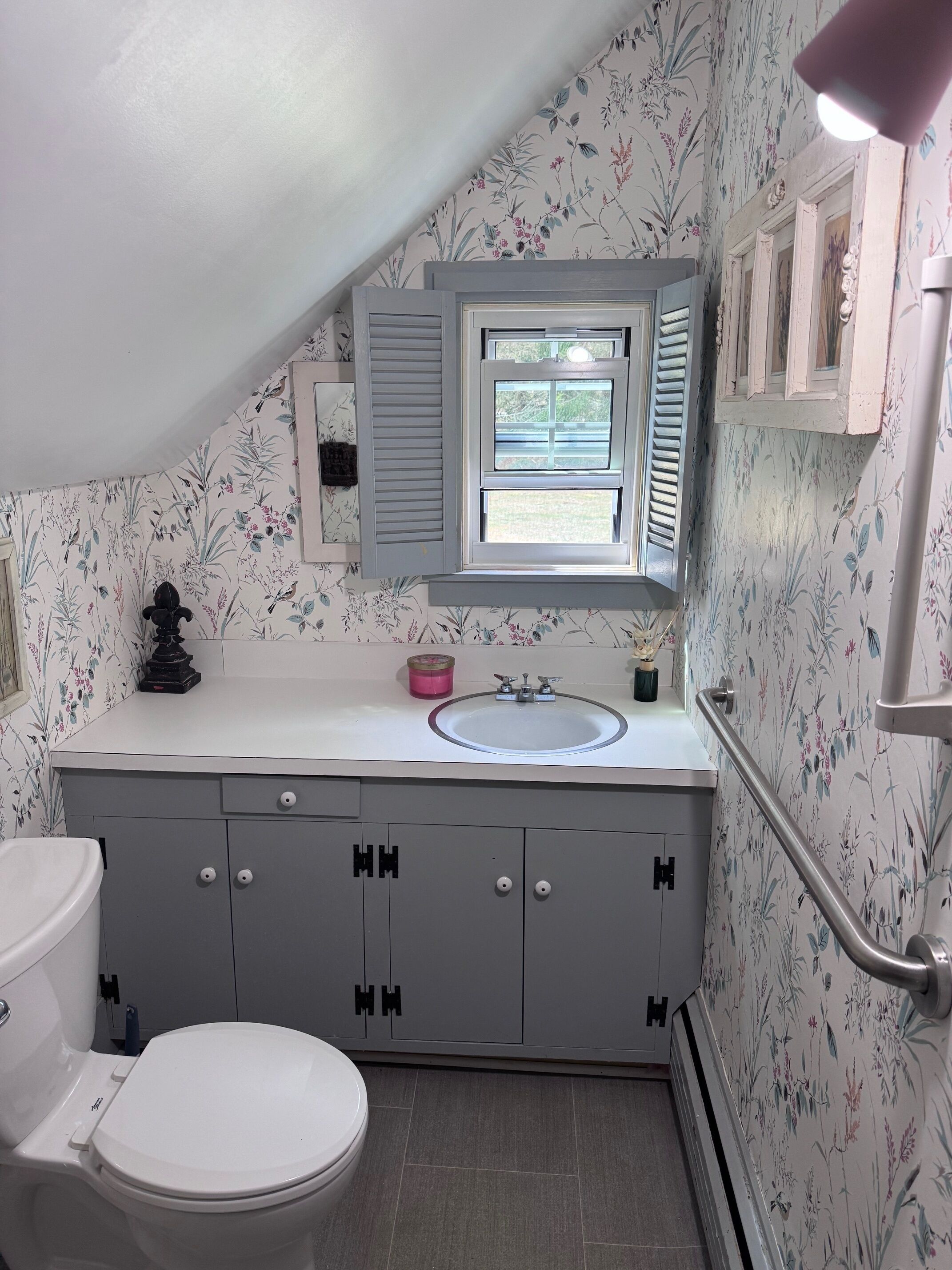 A bathroom with a toilet, a sink, and a window with shutters.
