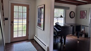 A hallway with a piano, a framed poster, and a door leading to a room with a window.