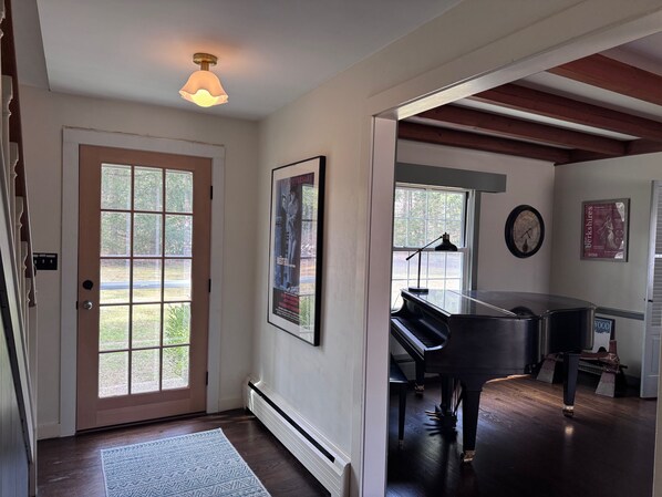 Un pasillo con un piano, un cartel enmarcado y una puerta que da a una habitación con ventana.