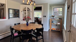 A dining area with a wooden table and chairs, a vase with flowers, and a ceiling light fixture.