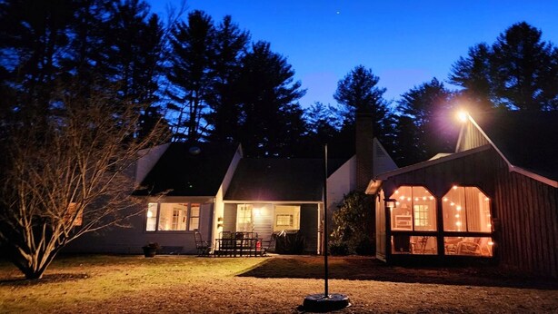 A house with a porch and a shed, both illuminated by lights.