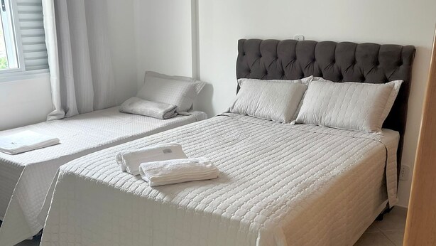Ein Hotelzimmer mit zwei Betten, einem großen Fenster mit Vorhängen und einem gefliesten Boden.