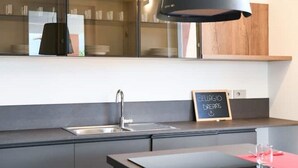 Une cuisine moderne avec un luminaire suspendu noir, un évier en acier inoxydable et un panneau noir où est écrit « CELLAGIO DREAMS ».