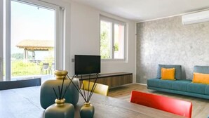 Un salon moderne avec une table en bois, un canapé agrémenté de coussins orange et un téléviseur posé sur un meuble.