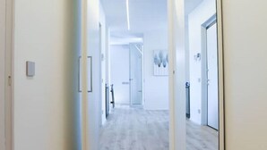 Un couloir moderne avec un plancher de couleur claire, des murs blancs et une porte en verre au fond.