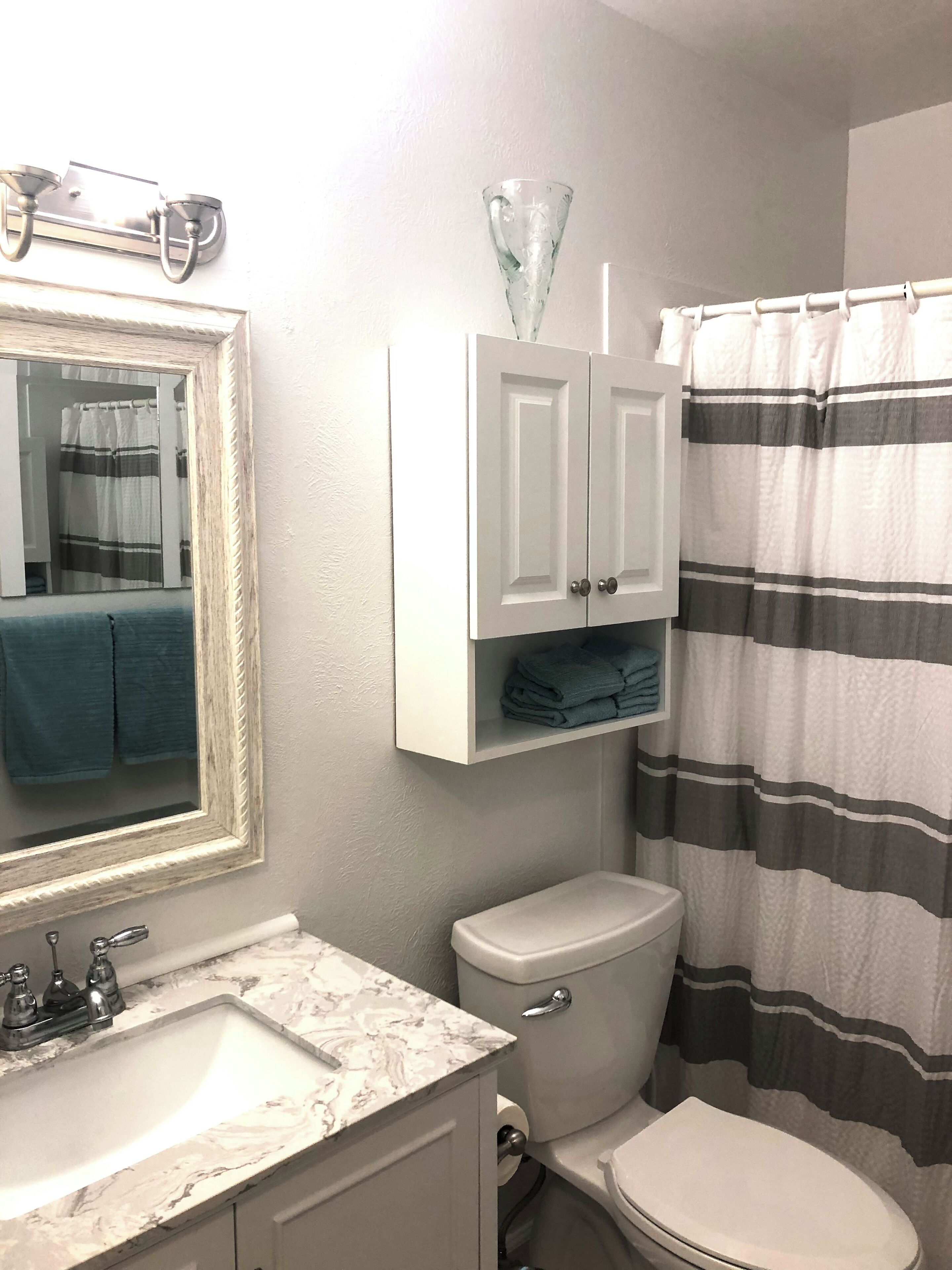 A bathroom with a marble sink, a toilet, a striped shower curtain, and a mirror with a towel hanging on it.