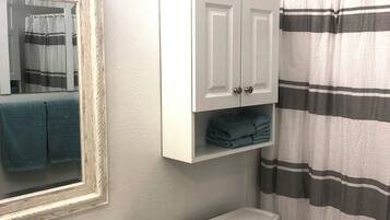 A bathroom with a marble sink, a toilet, a striped shower curtain, and a mirror with a towel hanging on it.