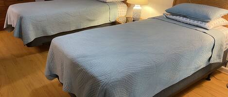 Dos camas individuales con cabeceras y pies de cama a juego, una mesita de noche con lámpara y un ventilador fijado a la pared.