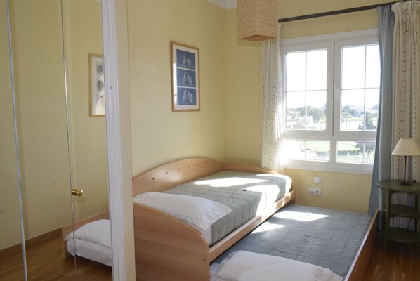 A bedroom with a single bed, a window with curtains, a small table with a lamp, and a framed picture on the wall. - Anacasa Atico MET Oliva Nova Golf AT1403 (Oliva)