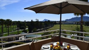 Un balcón con una mesa dispuesta para el desayuno, con vistas a un campo de golf y montañas.