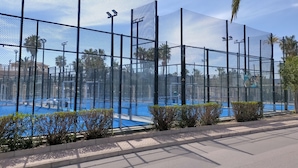 Una cancha de tenis cercada, con cielo despejado y palmeras al fondo.