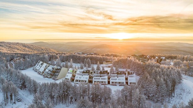 Une station de ski enneigée, dotée de plusieurs bâtiments, d’un télésiège et offrant un paysage montagneux en toile de fond.