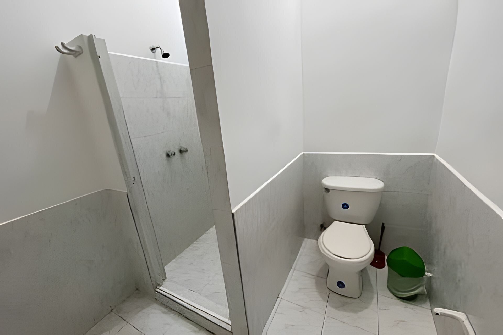 A bathroom with a shower, toilet, and a green trash bin.