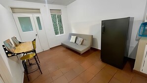Un espacio habitable compacto con sofá, una mesa de comedor con sillas, refrigerador y ventana con cortinas estampadas.