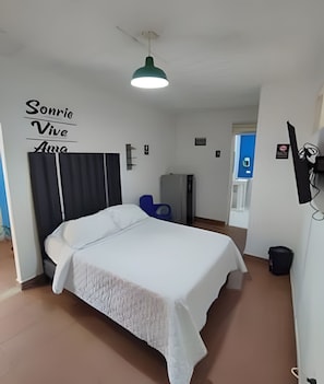 A bedroom with a bed, a wall-mounted TV, a ceiling light, and a sign with text. - Our Home San Antonio (Cali)