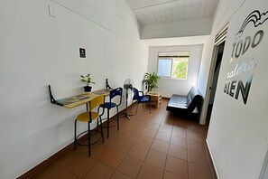 A room with a dining table, chairs, a sofa, a window, and a wall with a sign. - Our Home San Antonio (Cali)