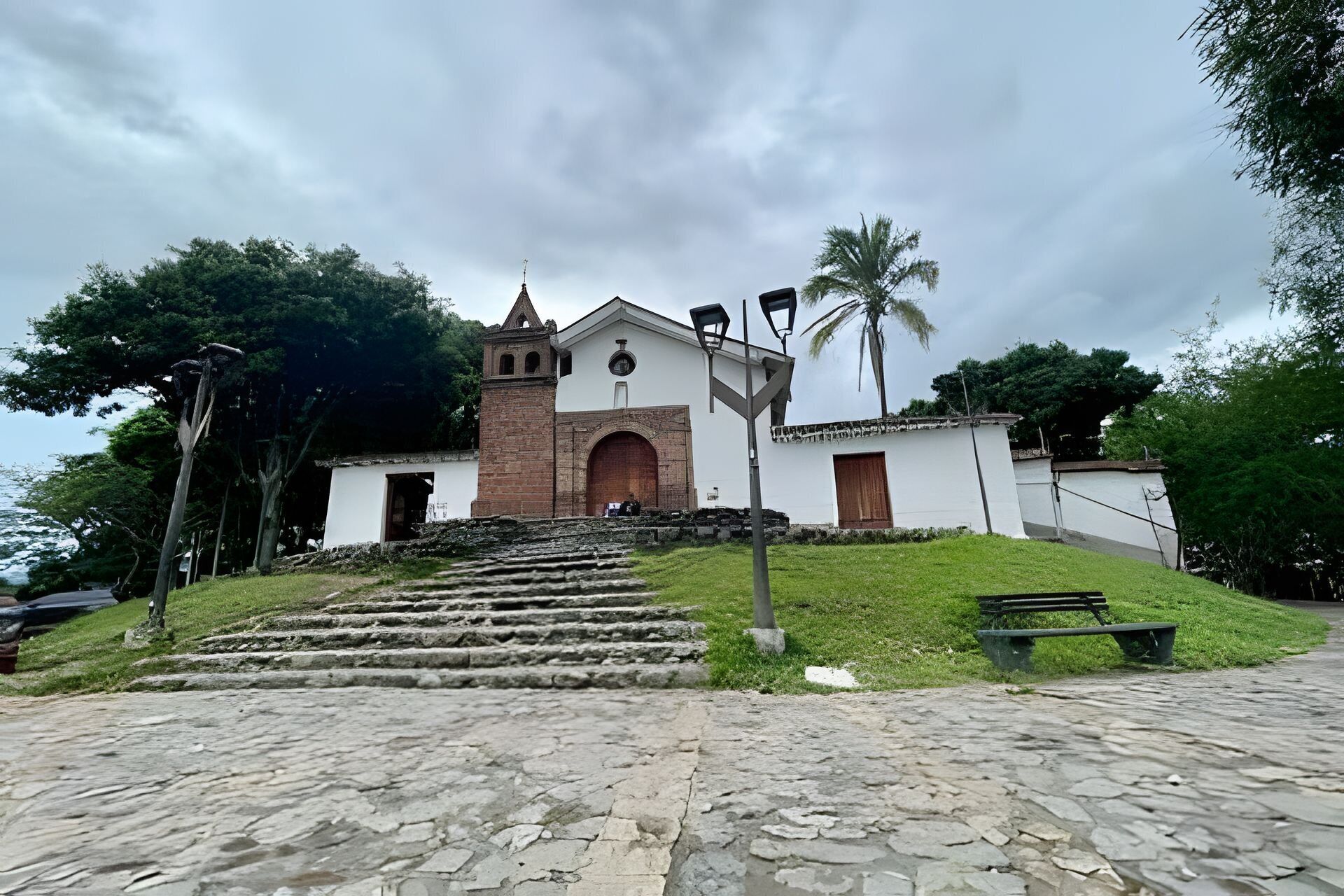 A church with a bell tower, steps leading up to it, and a palm tree in the background.