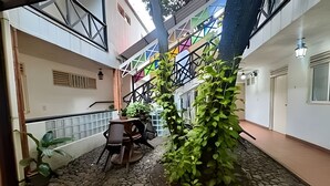 Un atrio de varios niveles con una escalera, una zona de estar con una mesa y sillas, y plantas en macetas.