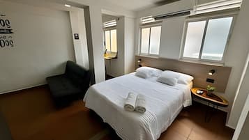 Een hotelkamer met een bed, een stoel, een nachtkastje met lamp en een raam.
