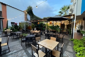 An outdoor cafe with tables and chairs, surrounded by greenery and a building. - Our Home San Antonio (Cali)