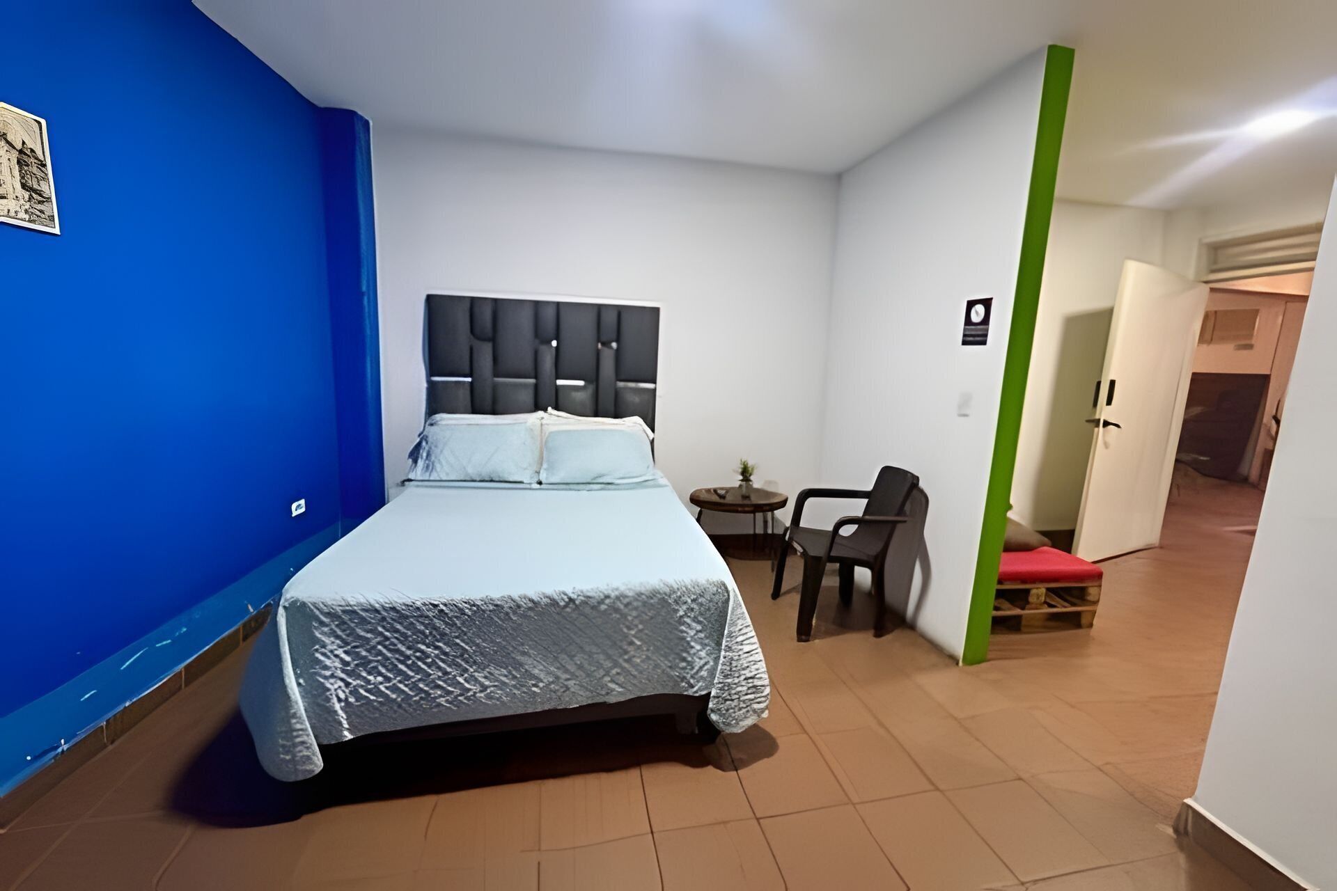 A hotel room with a bed, a small table, a chair, and a door leading to another room.