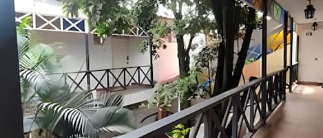 Un pasillo con un divisor de vidrio, plantas en macetas y vistas a árboles y un edificio al exterior.