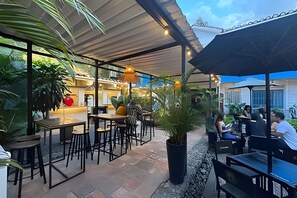 An outdoor cafe area with tables and chairs, surrounded by potted plants and a covered seating area. - Our Home San Antonio (Cali)