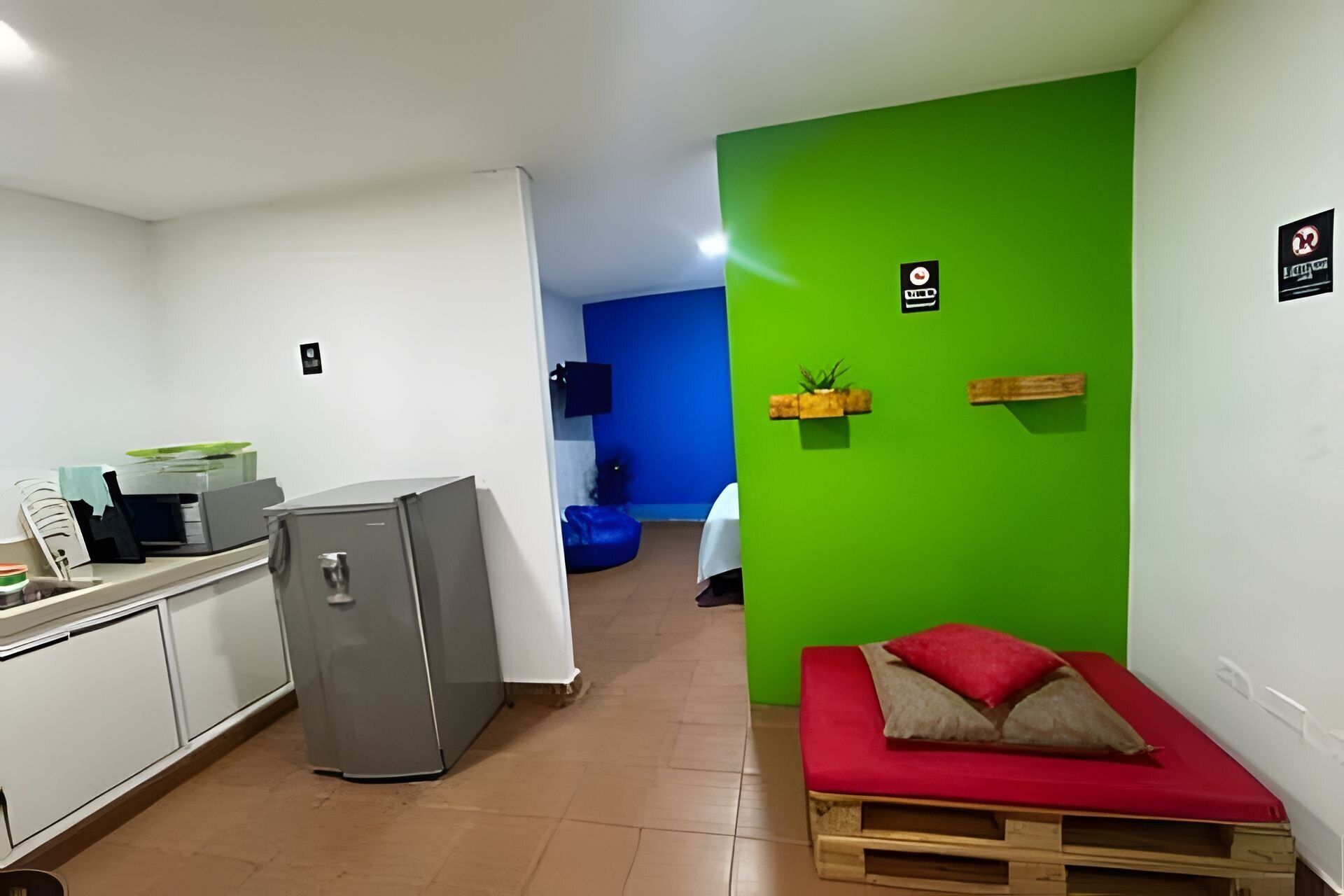 Une pièce dotée d’une kitchenette, d’un petit coin salon avec un coussin rouge et d’un mur d’accent vert.
