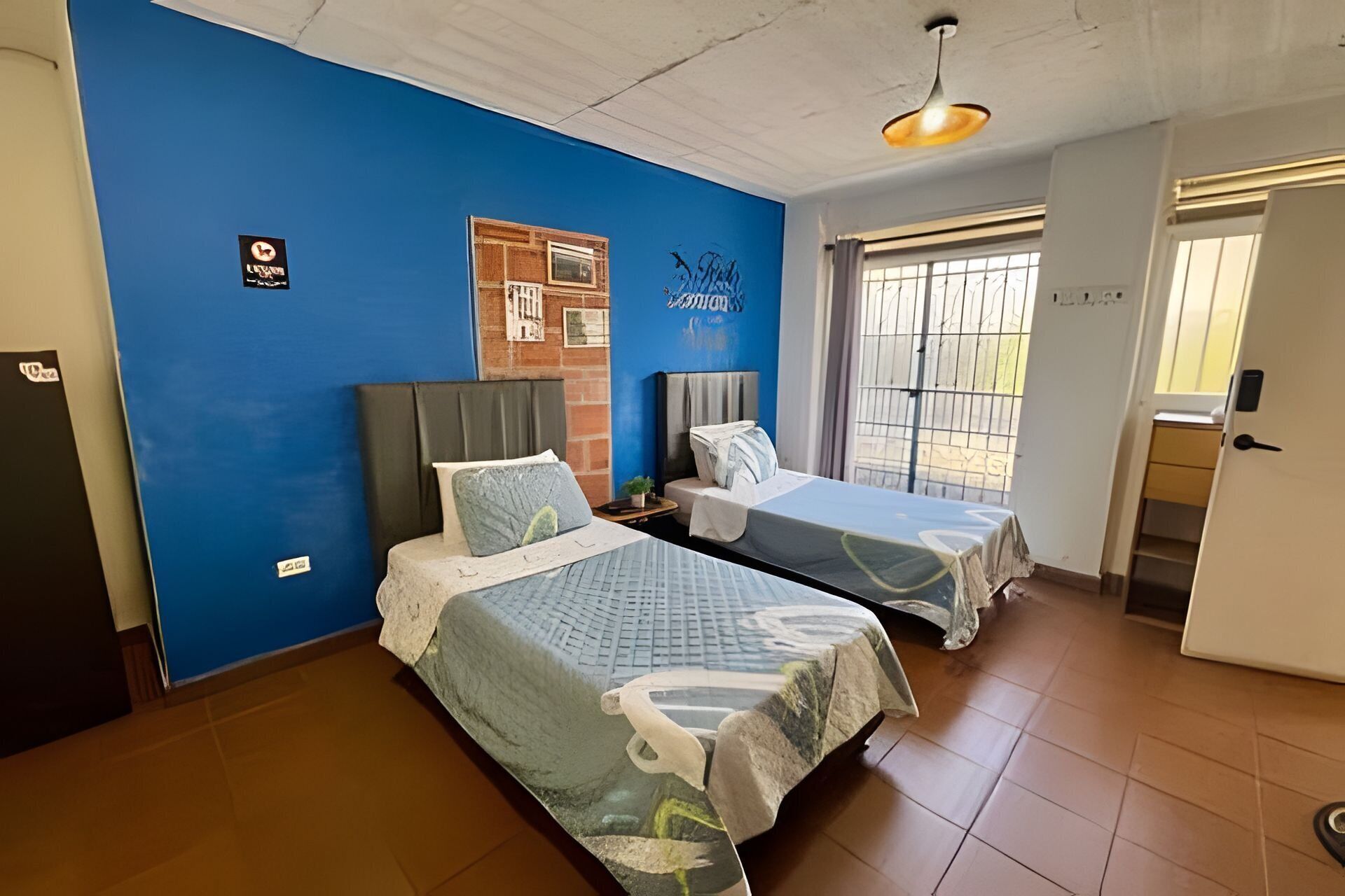 A room with two beds, a blue wall, a door, and a window.