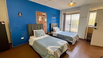 A room with two beds, a blue wall, a door, and a window.