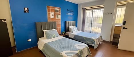 A room with two beds, a blue wall, a door, and a window.