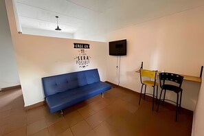 A room with a blue sofa, two chairs, a television mounted on the wall, and a ceiling fan. - Our Home San Antonio (Cali)
