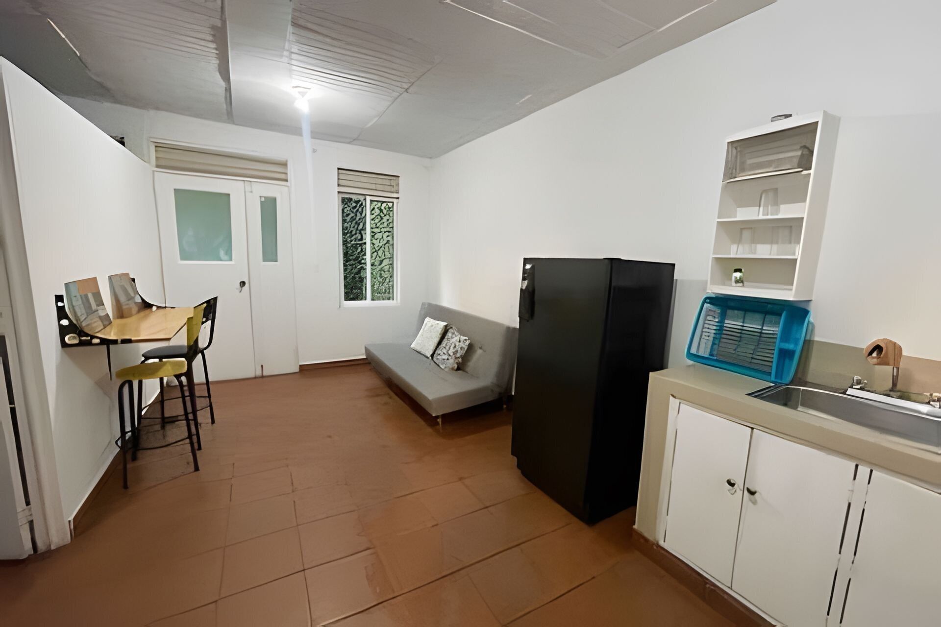 A compact kitchen with a refrigerator, a dining table with chairs, a sofa, and a small window with a view.