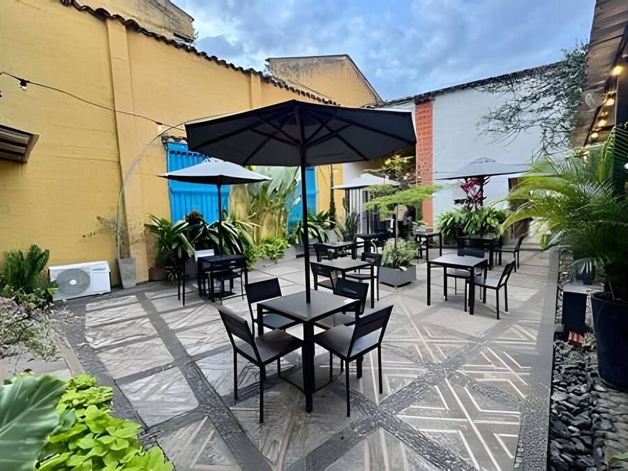 Une terrasse extérieure avec des tables et des chaises, entourée de plantes en pot et dotée d’un sol à motifs.