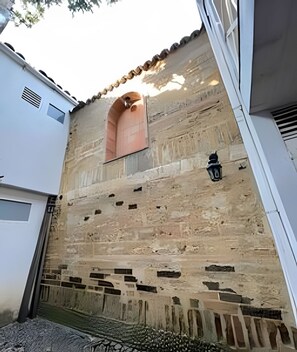 A building with a textured stone facade, a small arched window, and a black lantern. - Our Home San Antonio (Cali)