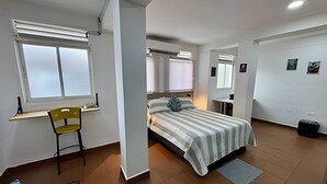 Un dormitorio con cama, escritorio, silla y ventana.