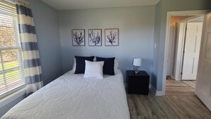 A bedroom with a bed, a nightstand, a window with curtains, and three wall-mounted pictures. - Abenaki Retreat on Matinicus Island (Matinicus)